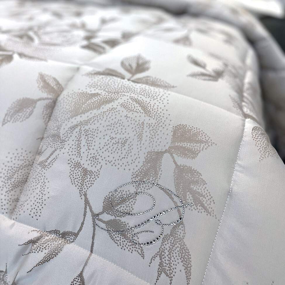 Trapunta Invernale matrimoniale Giorgia di Blumarine, in elegante raso jacquard. Romantica fantasia jacquard a tema floreale, colore ecrù, con logo Blumarine in preziosi cristalli Swarovski. dettaglio gantasia