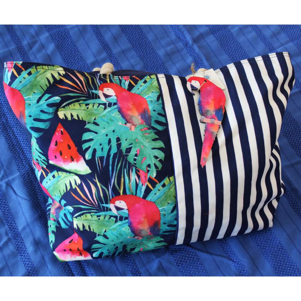 Uno stile unico anche in spiaggia, con la borsa da mare Karakorum Tropicalis. La borsa mare Tropicalis presenta una vivace fantasia per metà a righe verticali bianche e blu, e per metà con palme, pappagalli e angurie su fondo blu. La borsa è dotata di manici lunghi in corda. Chiusura con cerniera