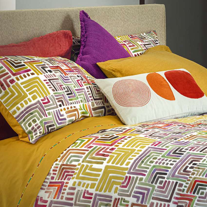 Completo lenzuola Fazzini Geometrie, in percalle di puro cotone. Disponibile per letto singolo e matrimoniale. Il lato superiore delle federe presenta una fantasia geometrica multicolore. Il resto del completo è in percalle di cotone tinta unita color ocra. Il lenzuolo di sopra è impreziosito da una codina multicolore.