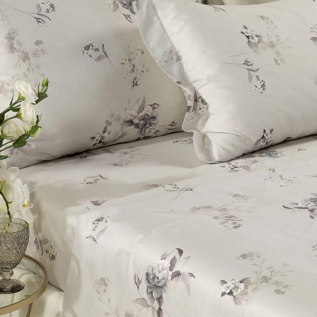 Completo lenzuola matrimoniale Caleffi Chiaro di Luna, in raso di puro cotone con stampa digitale. Fantasia con fiori dal colore delicato su fondo grigio/tortora chiaro. Federe in fantasia con due volant laterali.