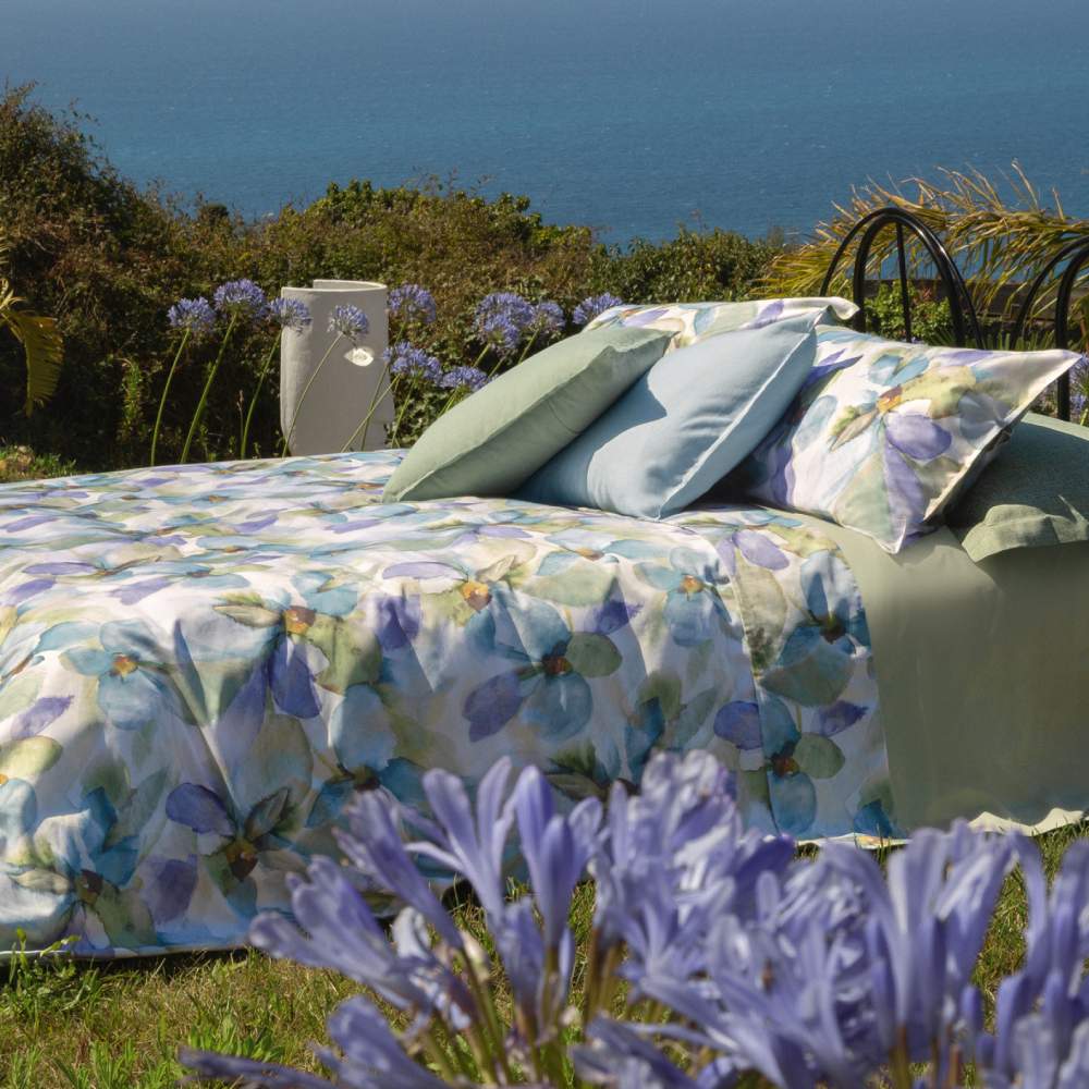 Lenzuolo copriletto matrimoniale Fazzini Trasparenze, in percalle di puro cotone. Il completo lenzuola Trasparenze ricrea, tramite la tecnica dell'acquerello, una luminosa fantasia floreale sui toni del verde e dell'azzurro. La fantasia è presente sulla faccia superiore delle federe a 4 volanini e sul lenzuolo di sopra. Anche la balza del lenzuolo di sopra è stampata, essendo un lenzuolo copriletto. Il resto del completo è il percalle di cotone tinta unita verde.