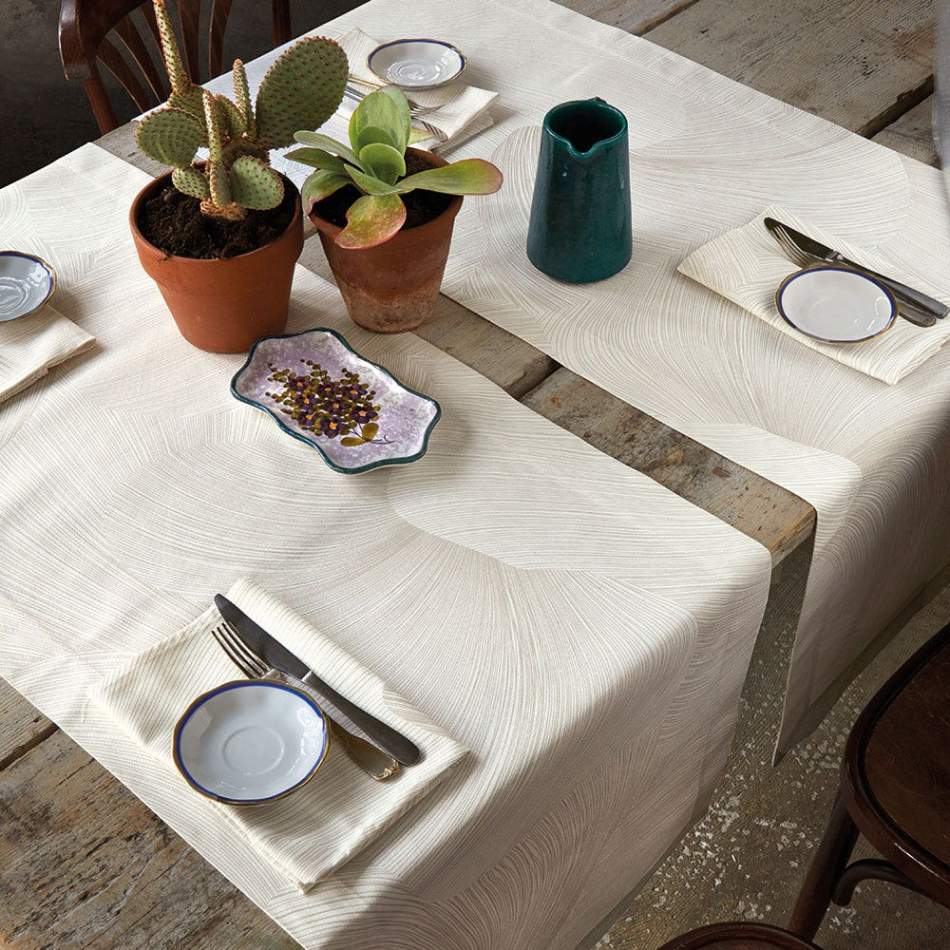 Runner Zante di Gabel Vallesusa, in raso di puro cotone stampato. Nella corsia Zante la raffinatezza del raso si unisce a pattern leggeri e geometrie indefinite, dalle forme morbide e sinuose, nella colorazione avorio/beige. Il set include una corsia rettangolare (50x150 cm) e due tovaglioli stampati (45x45 cm).