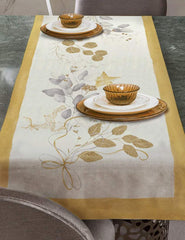 Corsia natalizia Mirage di Tessitura Randi. Stampata in digitale su tessuto di puro cotone. Il runner Mirage, con bordo ocra e fondo avorio, presenta una delicata fantasia con foglie, nastrini ed elementi tipici del Natale nei colori oro e grigio. Misura: 50x150 cm