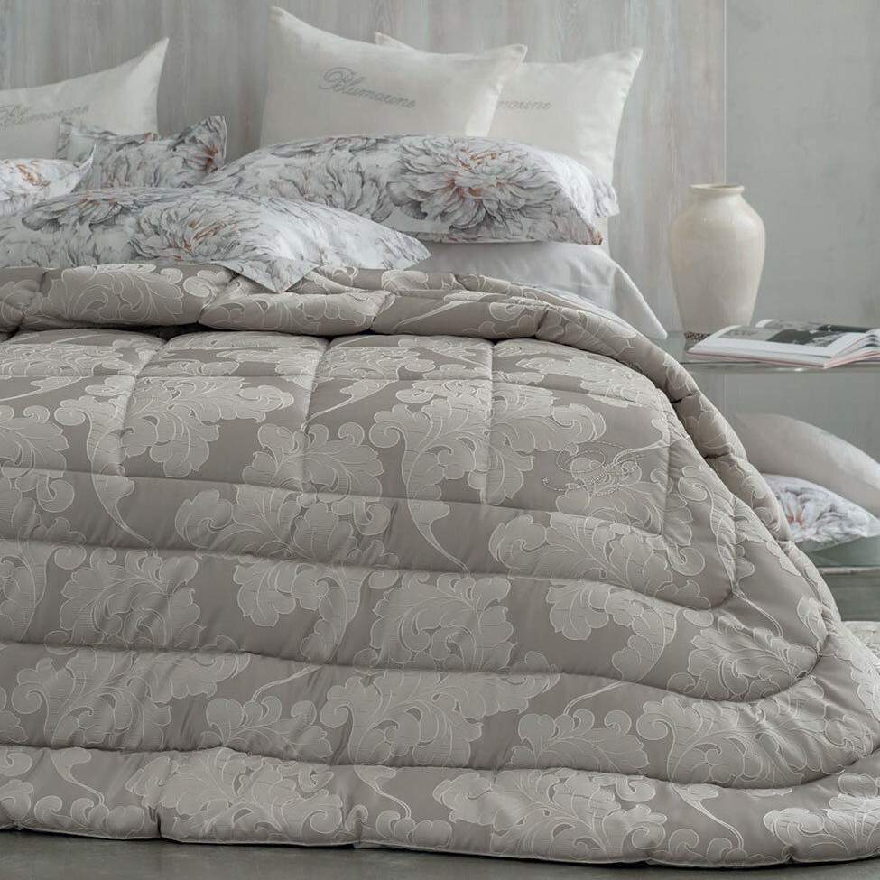 Trapunta Invernale matrimoniale Gemma di Blumarine, in elegante raso jacquard.Fantasia tinta in filo dalle forme morbide, nella variante di colore tortora, con logo Blumarine in preziosi cristalli Swarovski.