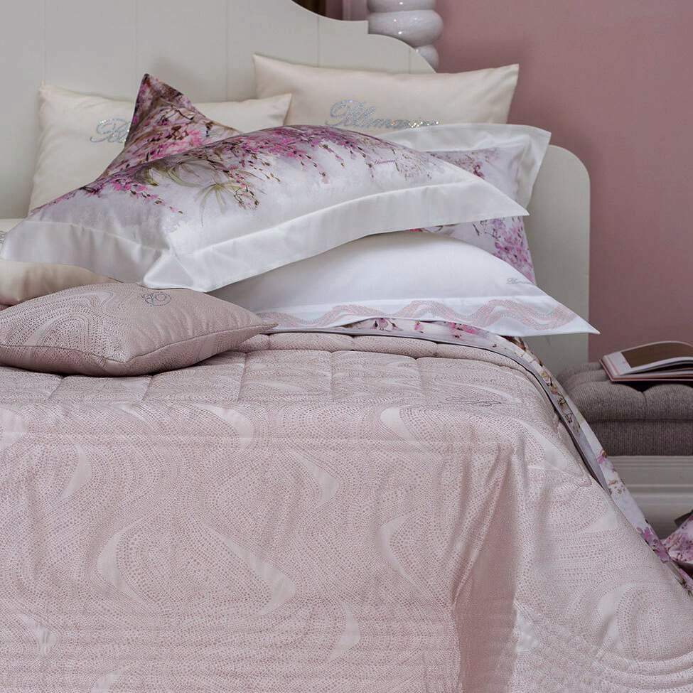 Trapuntino matrimoniale Crystelle di Blumarine, in elegante raso jacquard. Sinuosa fantasia jacquard dalle forme morbide, con inserti in lurex e logo Blumarine in cristalli. Disponibile nella variante di colore cipria rosa.