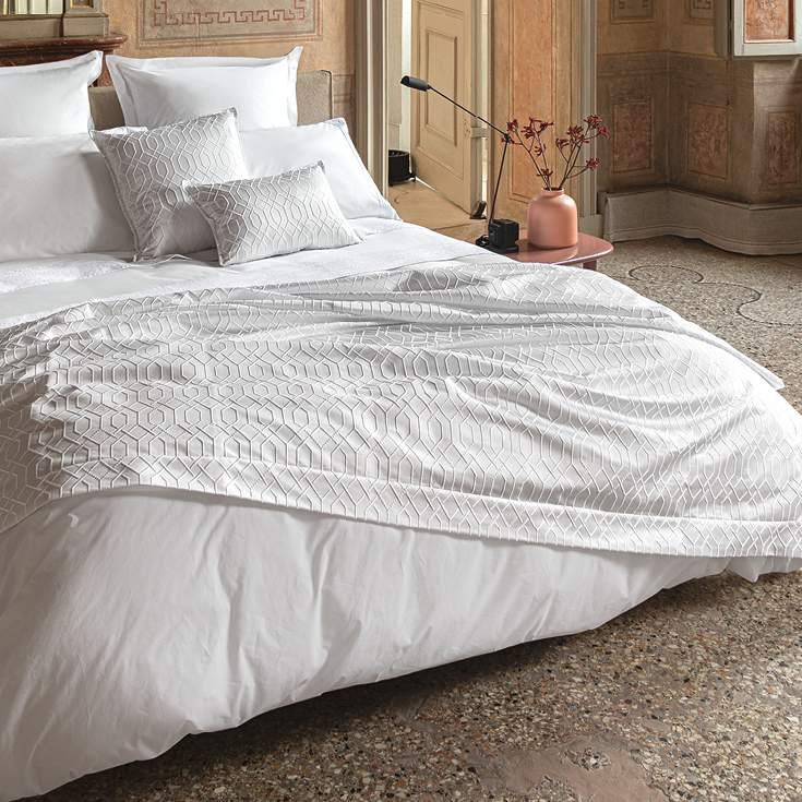 Trapuntino matrimoniale Villa Necchi, della linea Fazzini Atelier, in prezioso raso jacquard. Il quilt Villa Necchi presenta in un gioco tono su tono un bel motivo tridimensionale d'ispirazione dèco, con una mano morbida e voluminosa. Variante di colore champagne/avorio. La trapunta primaverile Villa Necchi è trapuntata a capo e rifinita a mano con due angoli sagomati che la adattano perfettamente agli angoli del letto