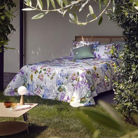 Trapunta primaverile matrimoniale Fazzini Camelia, in percalle di puro cotone. La fantasia floreale del trapuntino Camelia rende omaggio al fascino dei giardini italiani. Le camelie, le ortensie e le fresie fioriscono sulla superficie del quilt facendo incontrare in una delicata armonia il malva, l’azzurro e il bianco. La faccia superiore del trapuntino è in fantasia floreale, la faccia inferiore è tinta unita lilla.
