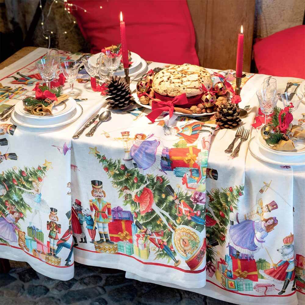 Tovaglia natalizia Schiaccianoci in puro lino di Tessitura Toscana Telerie. Fantasia piazzata su fondo chiaro, con abeti addobbati, regali e giocattoli che richiamano l'atmosfera del Natale. Misura rettangolare 170x270 cm.