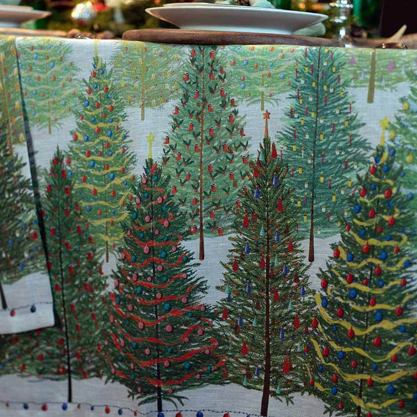 Tovaglia natalizia Fairy Trees in puro lino di Tessitura Toscana Telerie. Fantasia su fondo chiaro, con abeti verdi addobbati per il Natale. Misura rettangolare x12 (170x270 cm).
