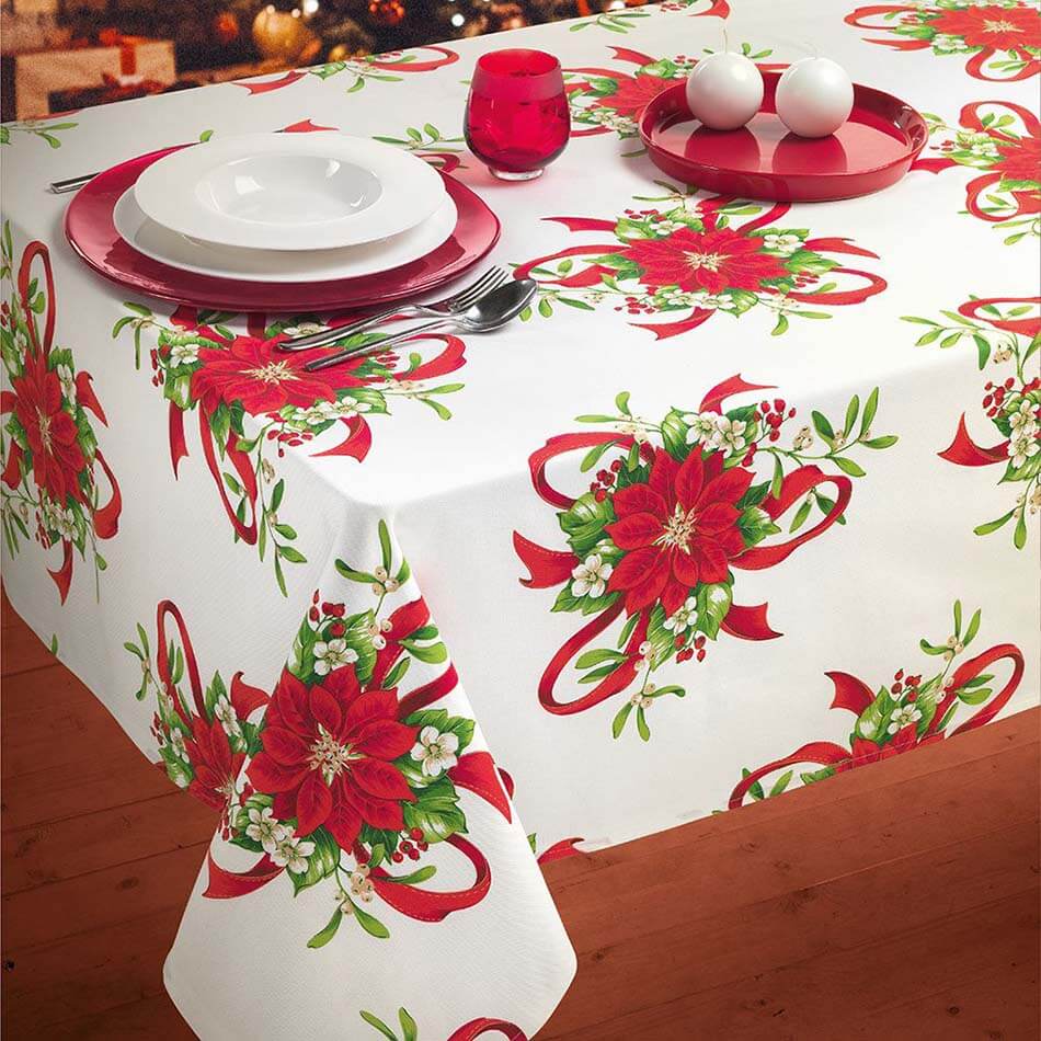 Tovaglia natalizia rettangolare Xmas Joy di Gabel. Fantasia floreale su fondo bianco. Il fondo e i fiori bianchi, le foglie verdi e i nastri, bacche e fiori rossi richiamano i tre colori che più di tutti rappresentano il Natale.