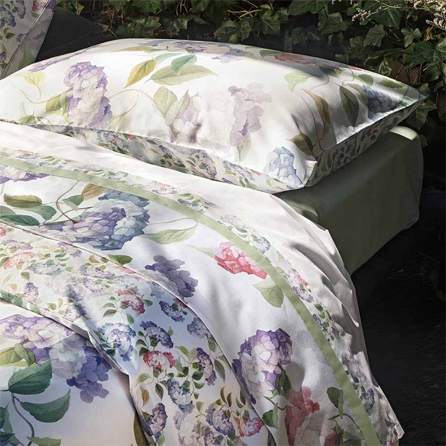 Completo Lenzuola matrimoniale Fazzini Ortensie in percalle di cotone. Fantasia floreale con fiori rosa e celesti sulle federe e sulla balza del lenzuolo di sopra. Lenzuolo di sotto in percalle tinta unita verde. Collezione primavera estate 2021.