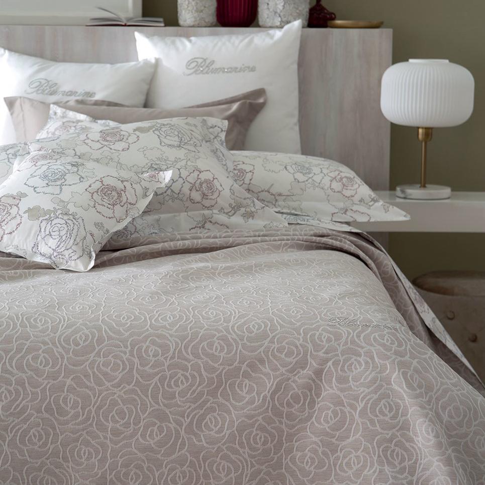 Copriletto estivo matrimoniale Leslie di Blumarine, in elegante raso jacquard. Romantica fantasia jacquard con linee sinuose che si intrecciano a formare delle rose, colore beige/tortora, con logo Blumarine in preziosi cristalli Swarovski. Coperta estiva