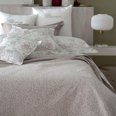 Copriletto estivo matrimoniale Leslie di Blumarine, in elegante raso jacquard. Romantica fantasia jacquard con linee sinuose che si intrecciano a formare delle rose, colore beige/tortora, con logo Blumarine in preziosi cristalli Swarovski. Coperta estiva