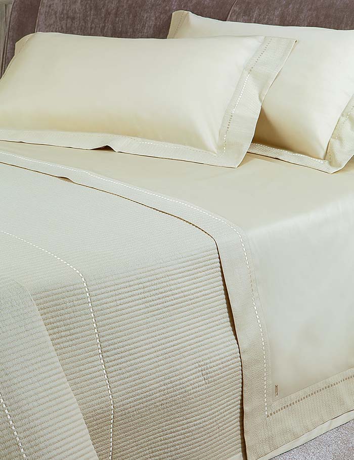 Completo lenzuola matrimoniale Borbonese New York in raso di puro cotone 300 T.C.. Variante di colore sabbia. Il completo lenzuola Borbonese New York è confezionato con lista ricamata sulla balza del lenzuolo di sopra e sui volant delle federe. Ha un look sobrio ma elegante ed è impreziosito da placchetta di metallo con logo Borbonese.