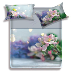 Lenzuolo copriletto matrimoniale Nura di Miss Terry Biancaluna in puro cotone. Il completo lenzuola Nura è stampato in digitale ad alta definizione. Le federe e il lenzuolo di sopra presentano una fantasia floreale con fiori bianchi su fondo azzurro/verde acqua. Le lenzuola con angoli e la balza del lenzuolo di sopra sono in tinta unita color grigio