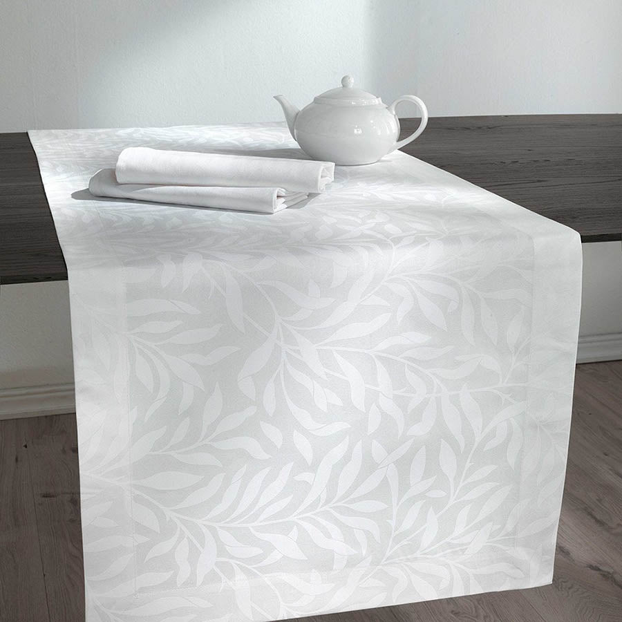 Runner Isabelle di Somma, in twill di puro cotone stampato. Il set include una corsia rettangolare (50x150 cm) e due tovaglioli stampati (45x45 cm). Corsia con fantasia floreale tono su tono, foglie bianche su fondo chiaro.