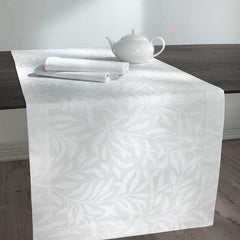 Runner Isabelle di Somma, in twill di puro cotone stampato. Il set include una corsia rettangolare (50x150 cm) e due tovaglioli stampati (45x45 cm). Corsia con fantasia floreale tono su tono, foglie bianche su fondo chiaro.