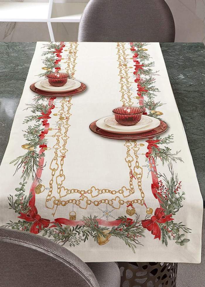 Corsia natalizia Charms di Tessitura Randi. Stampata in digitale su tessuto di puro cotone. Runner in fantasia, fondo avorio con particolari catenine dorate ed elementi tipici del Natale come ghirlande e fiocchi rossi. Misura: 50x150 cm