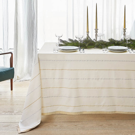 Tovaglia natalizia Wish di Fazzini, misura rettangolare per 12 persone. Tessuto tinto in filo di cotone e lurex con bordo dorato. Fantasia su fondo avorio con righe oro e argento che riprendono i colori del Natale. Misura rettangolare per 12 persone (180x295 cm).