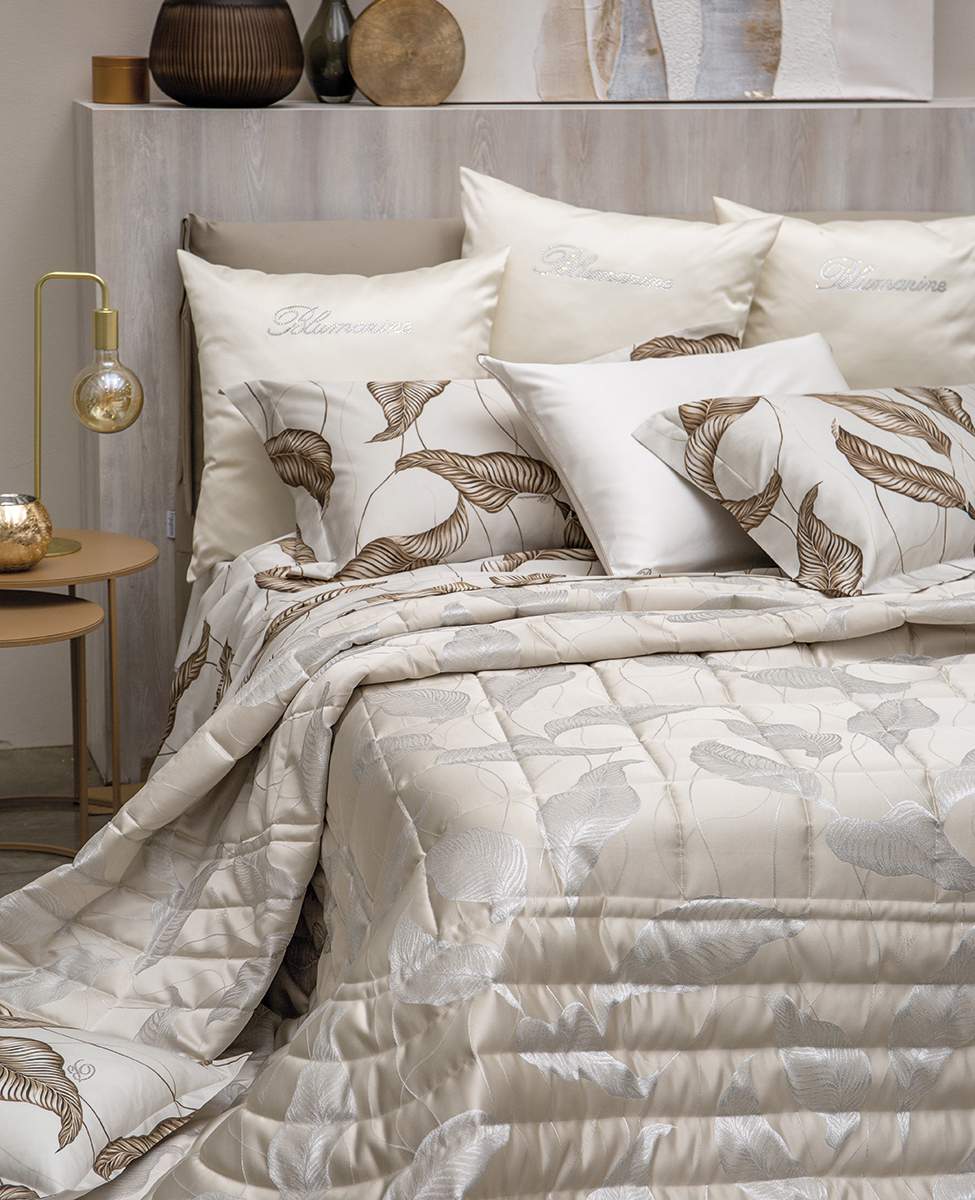 Trapuntino matrimoniale Luce di Blumarine, in elegante raso jacquard. Trapunta primaverile con elegante fantasia jacquard con foglie argentate che risaltano sul fondo tinta unita burro avorio. Copriletto trapuntato, quilt. Il ogo Blumarine è tinto in filo nella trama del tessuto.