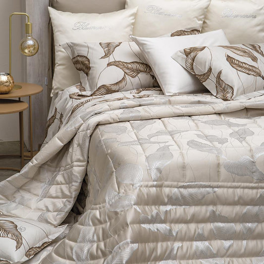 Trapuntino matrimoniale Luce di Blumarine, in elegante raso jacquard. Trapunta primaverile con elegante fantasia jacquard con foglie argentate che risaltano sul fondo tinta unita burro avorio. Copriletto trapuntato, quilt. Il ogo Blumarine è tinto in filo nella trama del tessuto.