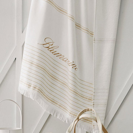 Telo mare Blumarine Isola, in spugna di puro cotone.  Telo mare elegante e raffinato, con logo Blumarine ricamato e righe dorate tinte in filo su fondo avorio. Fronte liscio e retro in micro spugna di cotone.  Spugna di cotone idrofilo da 300 g/mq.  Misura: 100x180 cm.