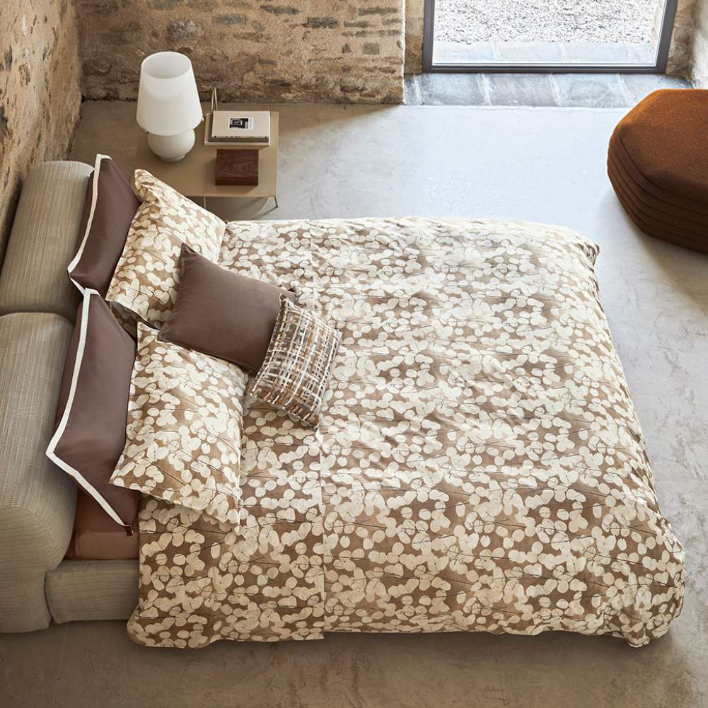 Copripiumino matrimoniale Fazzini Lunaria, in percalle di puro cotone. Il copripiumino Lunaria presenta una fantasia floreale dallo stile moderno, con fiori chiari su fondo tortora/cammello. Il set include un sacco copripiumino e due federe