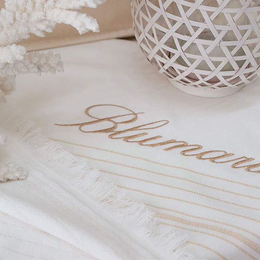 Telo mare Blumarine Isola, in spugna di puro cotone.  Telo mare elegante e raffinato, con logo Blumarine ricamato e righe dorate tinte in filo su fondo avorio. Fronte liscio e retro in micro spugna di cotone.  Spugna di cotone idrofilo da 300 g/mq.  Misura: 100x180 cm.