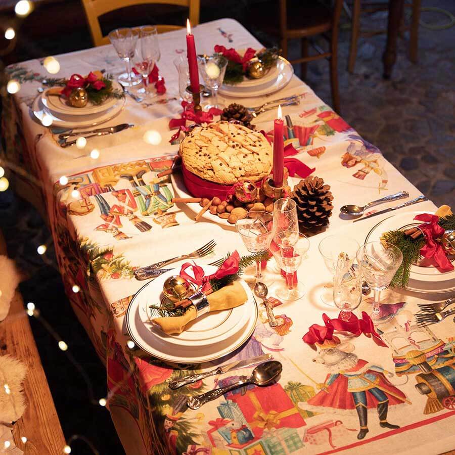 Tovaglia natalizia Schiaccianoci in puro lino di Tessitura Toscana Telerie. Fantasia piazzata su fondo chiaro, con abeti addobbati, regali e giocattoli che richiamano l'atmosfera del Natale. Misura rettangolare 170x270 cm.
