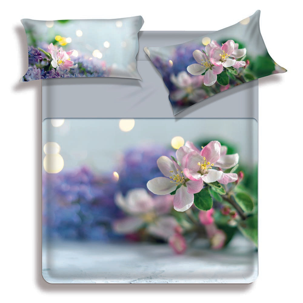 Lenzuolo copriletto matrimoniale Nura di Miss Terry Biancaluna in puro cotone.  Il completo lenzuola Nura è stampato in digitale ad alta definizione. Le federe e il lenzuolo di sopra presentano una fantasia floreale con fiori bianchi su fondo azzurro/verde acqua. Le lenzuola con angoli e la balza del lenzuolo di sopra sono in tinta unita color grigio