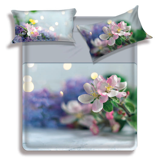 Lenzuolo copriletto matrimoniale Nura di Miss Terry Biancaluna in puro cotone.  Il completo lenzuola Nura è stampato in digitale ad alta definizione. Le federe e il lenzuolo di sopra presentano una fantasia floreale con fiori bianchi su fondo azzurro/verde acqua. Le lenzuola con angoli e la balza del lenzuolo di sopra sono in tinta unita color grigio