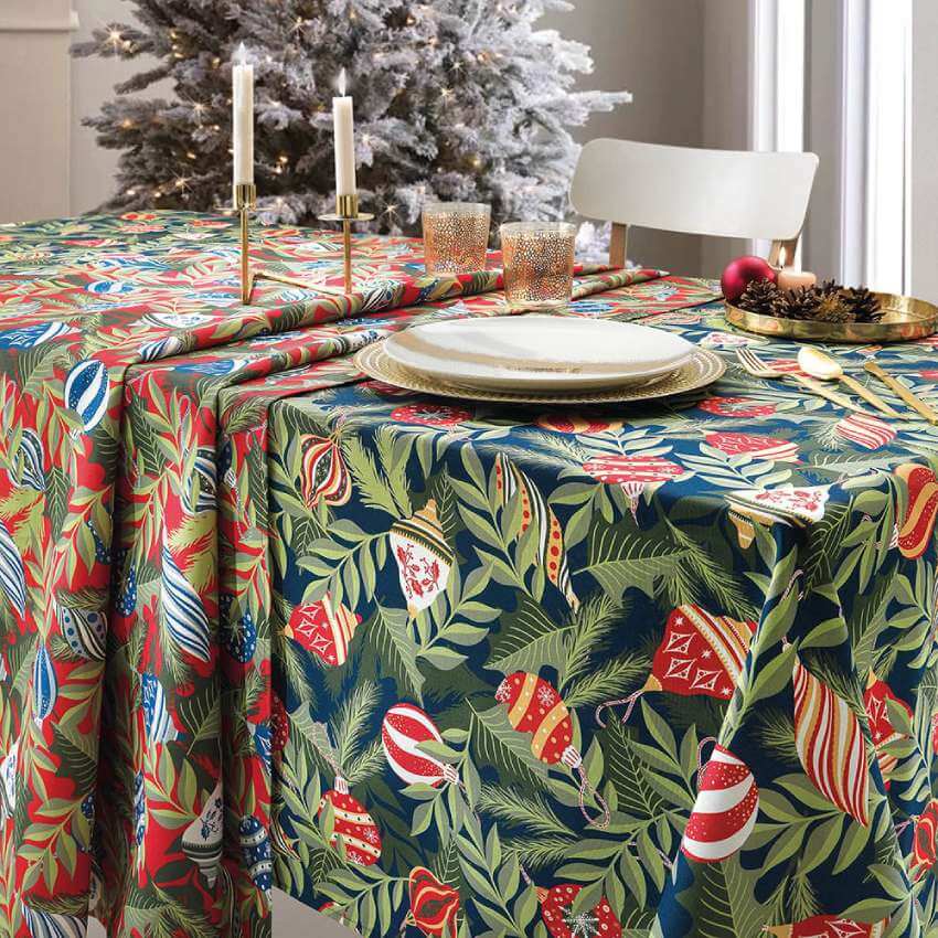 Tovaglia di Natale Adorn di Gabel, in panama di puro cotone.   Fantasia originale che rievoca i colori e le forme della tradizione natalizia. Fondo rosso con foglie verdi e sfere azzurre.