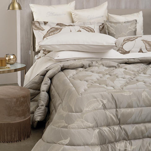 Trapuntino matrimoniale Luce di Blumarine, in elegante raso jacquard. Trapunta primaverile con elegante fantasia jacquard con foglie dorate che risaltano sul fondo tinta unita tortora. Copriletto trapuntato, quilt. Il ogo Blumarine è tinto in filo nella trama del tessuto.
