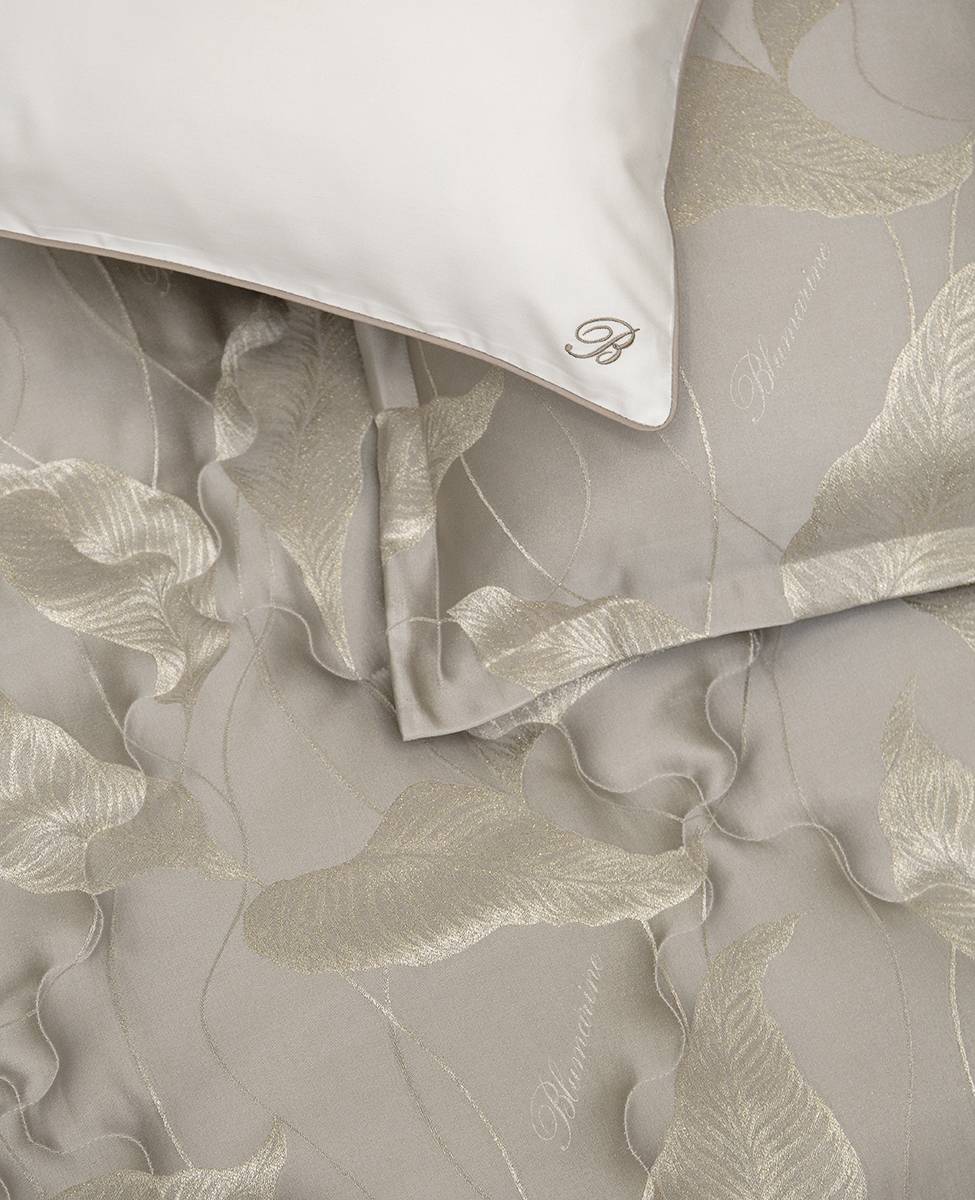 Trapuntino matrimoniale Luce di Blumarine, in elegante raso jacquard. Trapunta primaverile con elegante fantasia jacquard con foglie dorate che risaltano sul fondo tinta unita tortora. Copriletto trapuntato, quilt. Il ogo Blumarine è tinto in filo nella trama del tessuto.